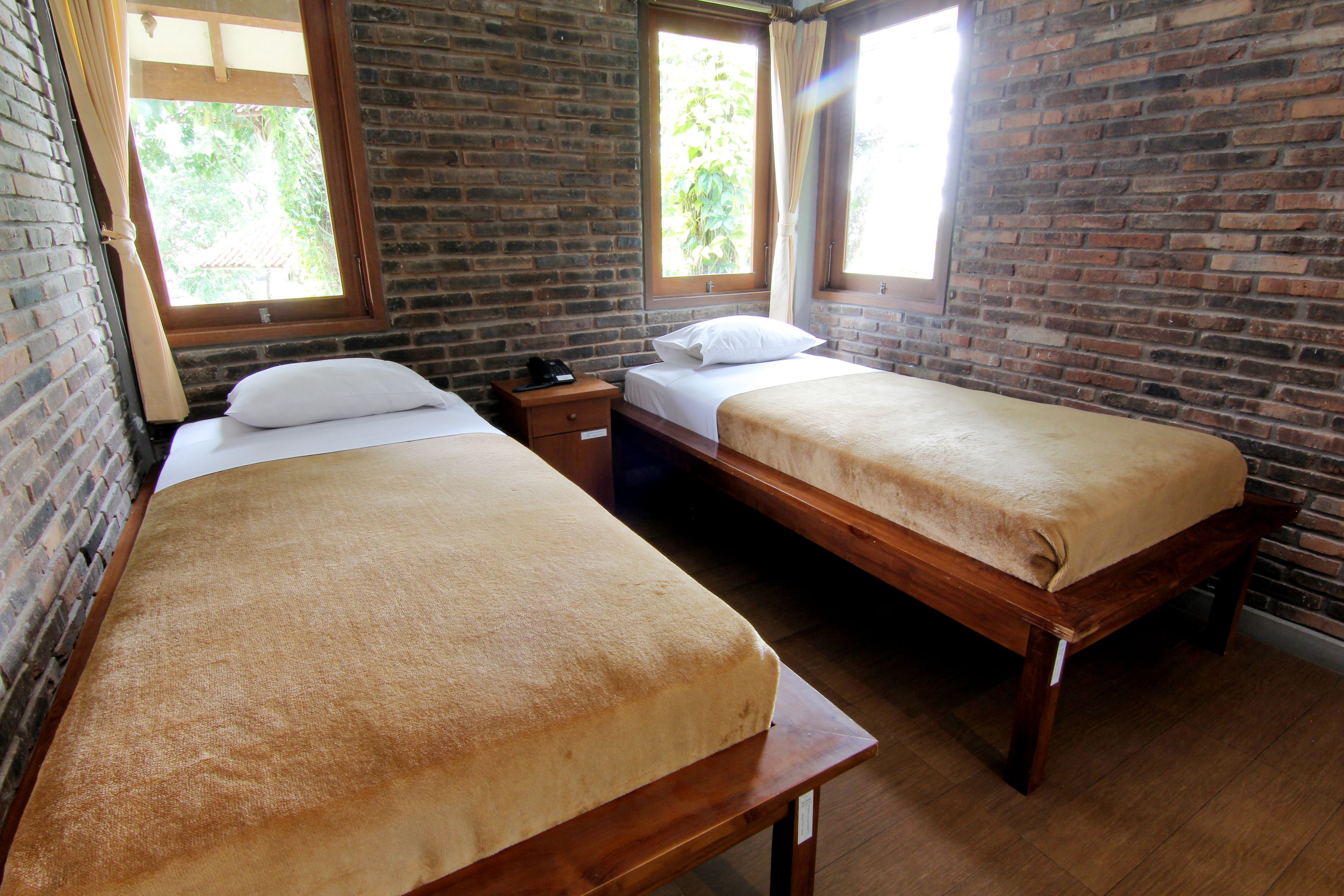 A room with two wooden beds, a brick wall, and windows with curtains.