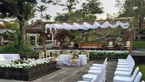 An outdoor wedding venue with rows of white chairs, tables, and a decorated archway. - Disaster Oasis (Pakem)