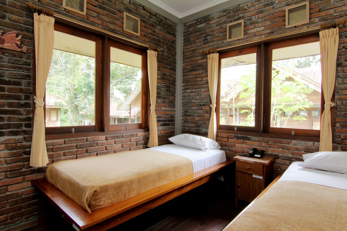 A room with two beds, a wooden bench, a nightstand, and brick walls.
