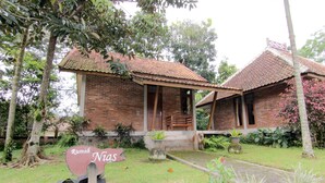 A traditional brick house with a tiled roof, surrounded by lush greenery and a sign that reads "Rumah Nias." - Disaster Oasis (Pakem)