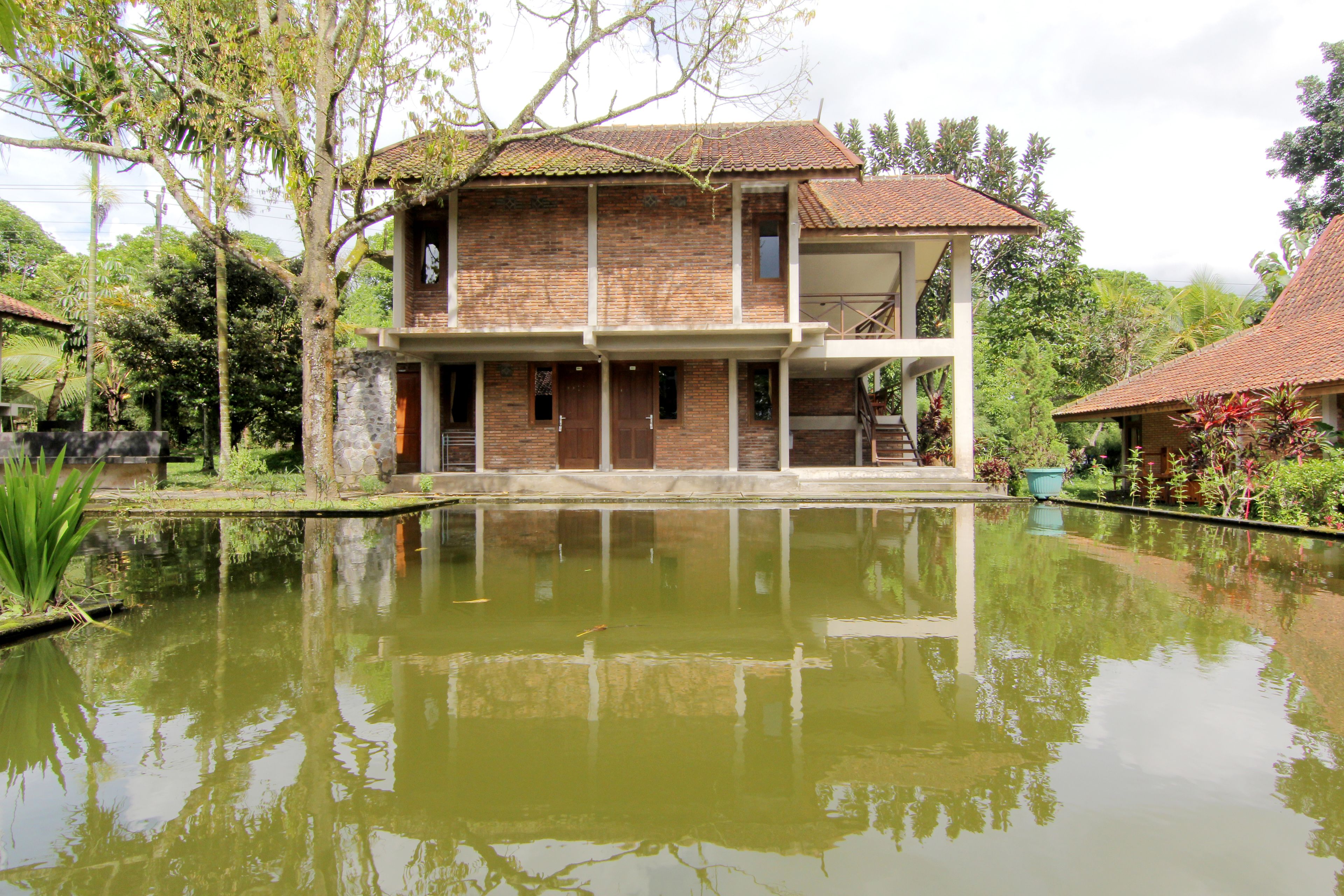 A two-story house with a balcony, a pond in front, and a garden.