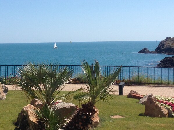 A coastal view with a clear sky, a sandy beach, and a rocky outcrop.