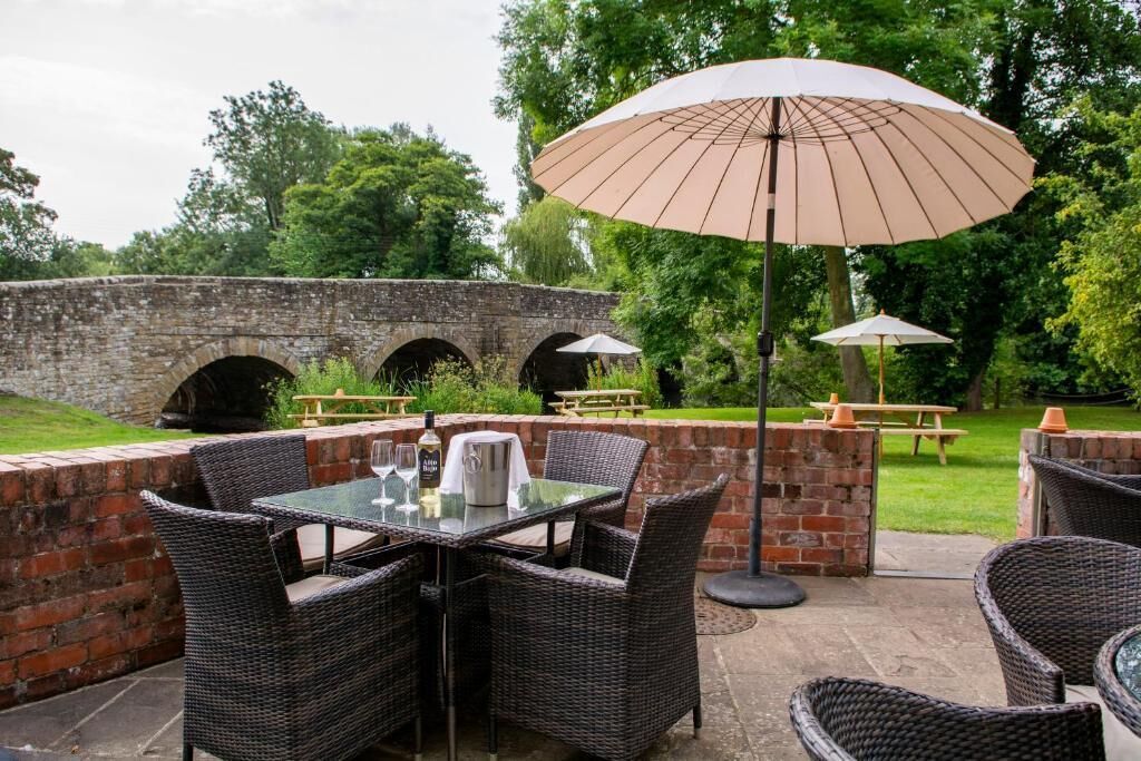 Un espace extérieur aménagé en terrasse, avec des meubles en osier et une table dressée pour les repas, le tout entouré de murs en briques et de verdure.