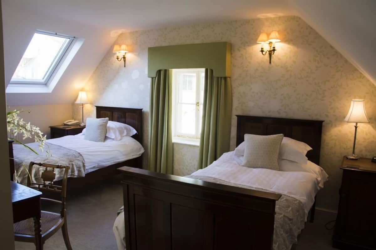 A room with two beds, a desk, a chair, a window, and a door.