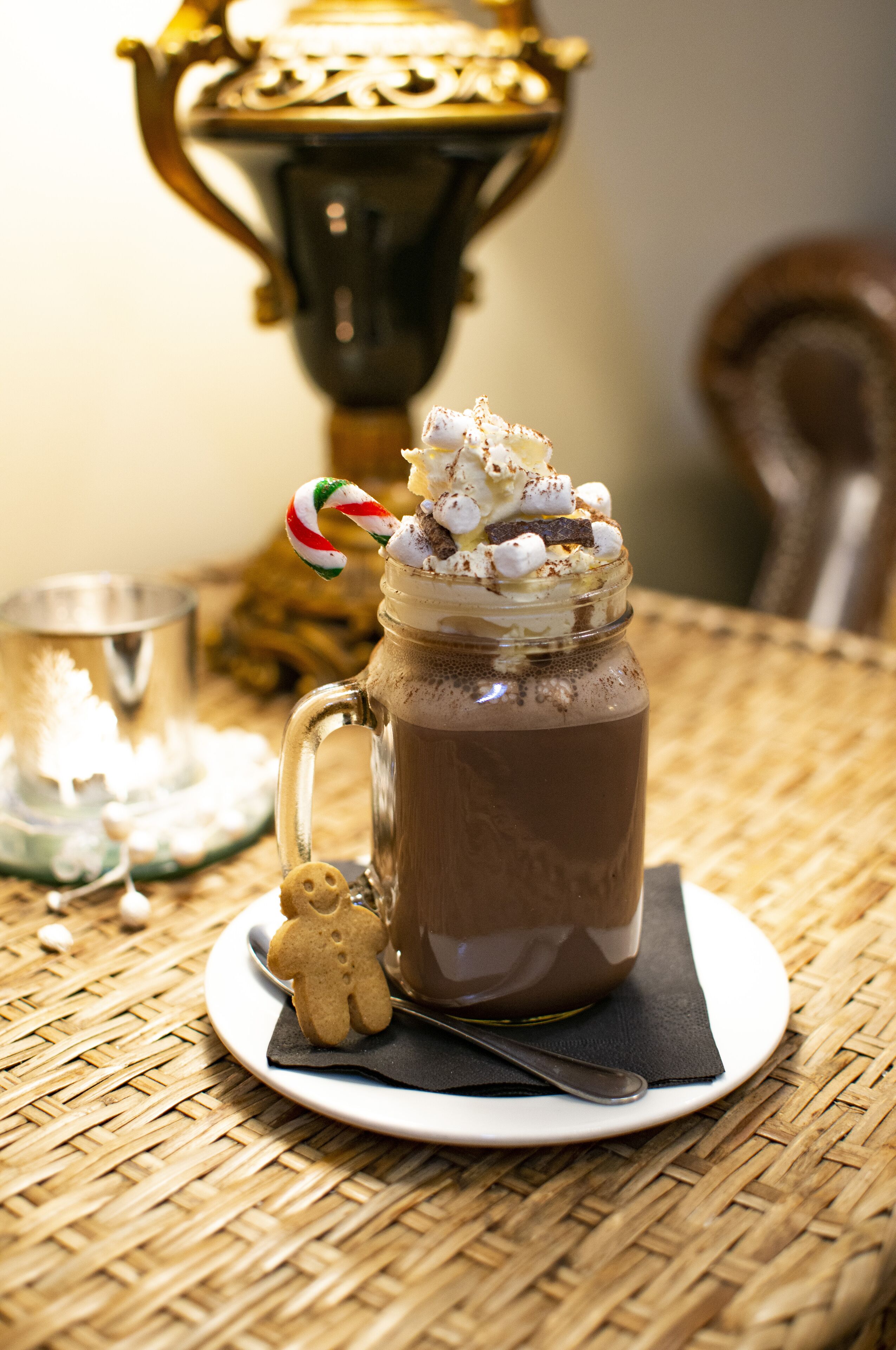 Una taza de chocolate caliente con malvaviscos y un bastón de caramelo sobre un plato, una cuchara y una galleta de hombre de jengibre.