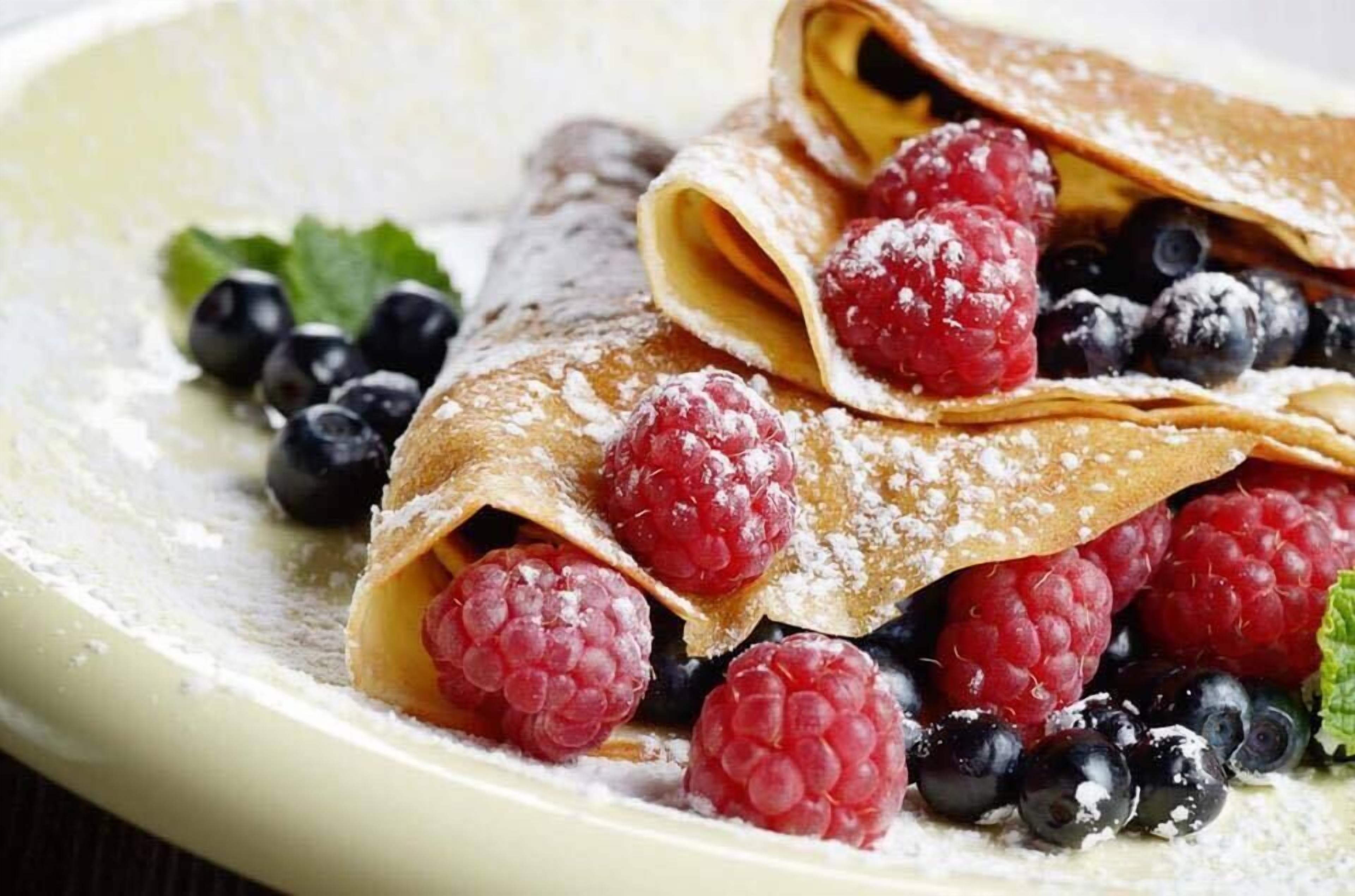 Un plato de crepas con frambuesas y arándanos, espolvoreadas con azúcar glas.