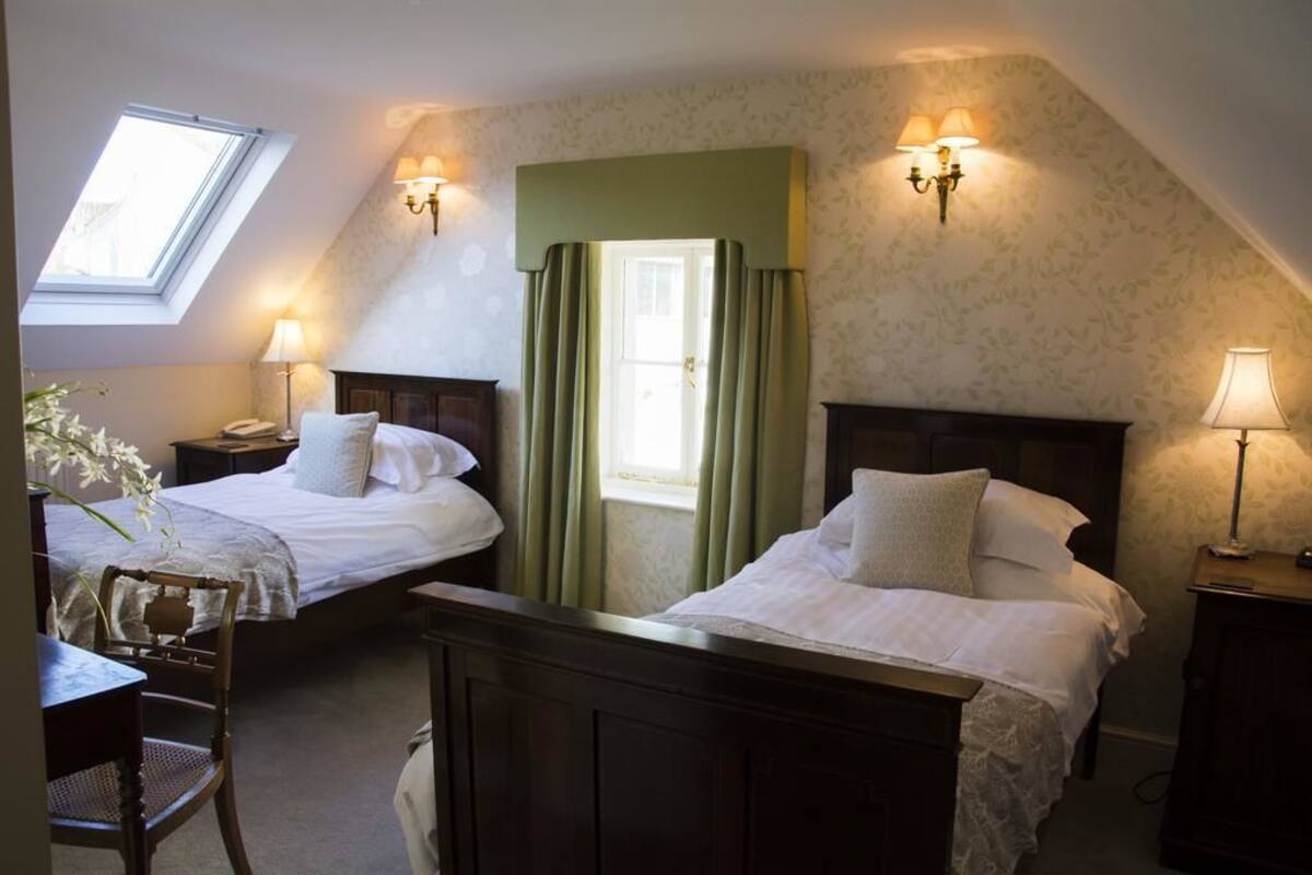 A room with two beds, a desk, and a chair. There is a window with a view of the outside.