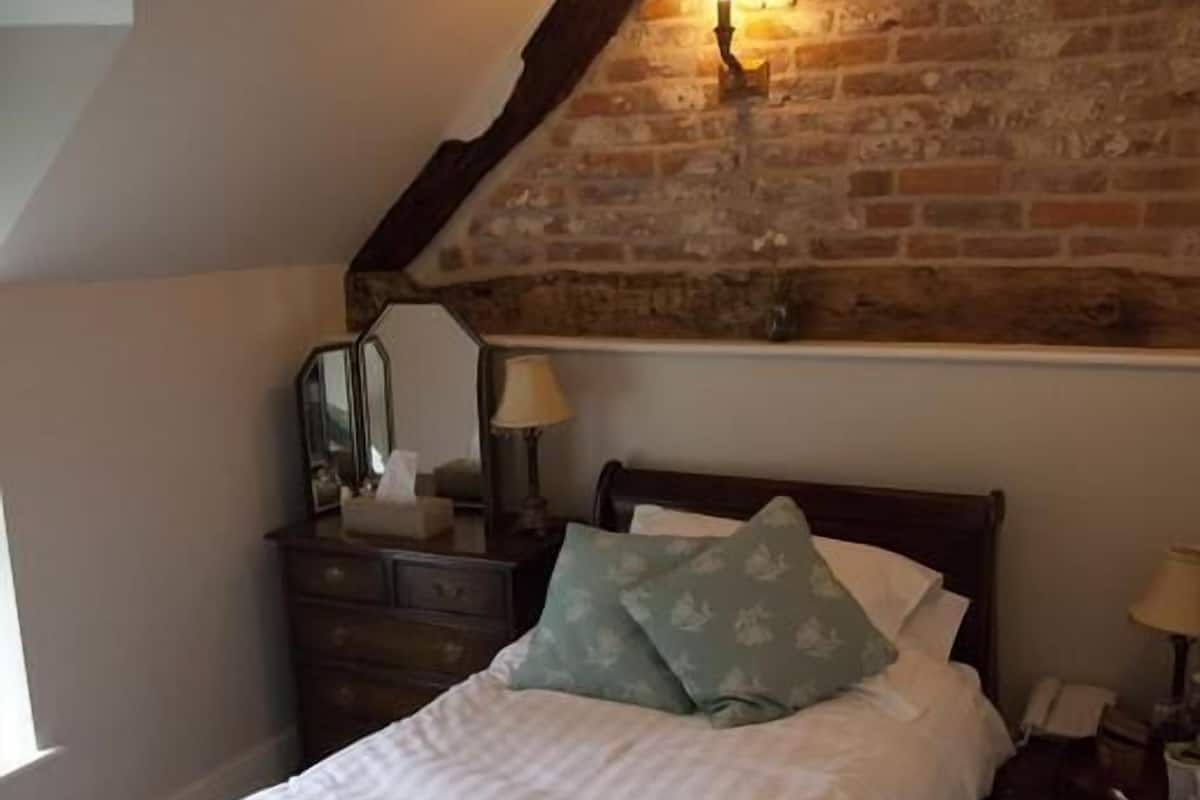 A bedroom with a wooden bed, a nightstand, a dresser, and a brick wall.