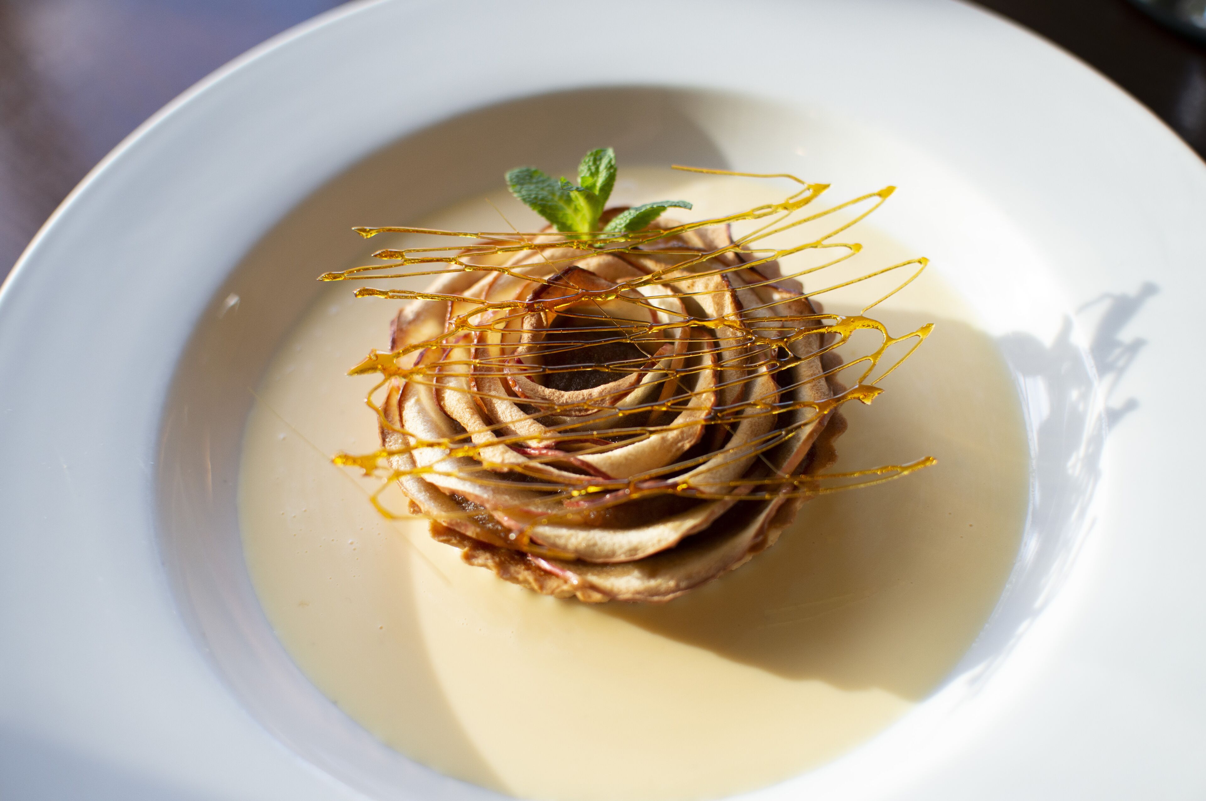 Un postre en un plato blanco, adornado con una hoja de menta y finas hebras amarillas.