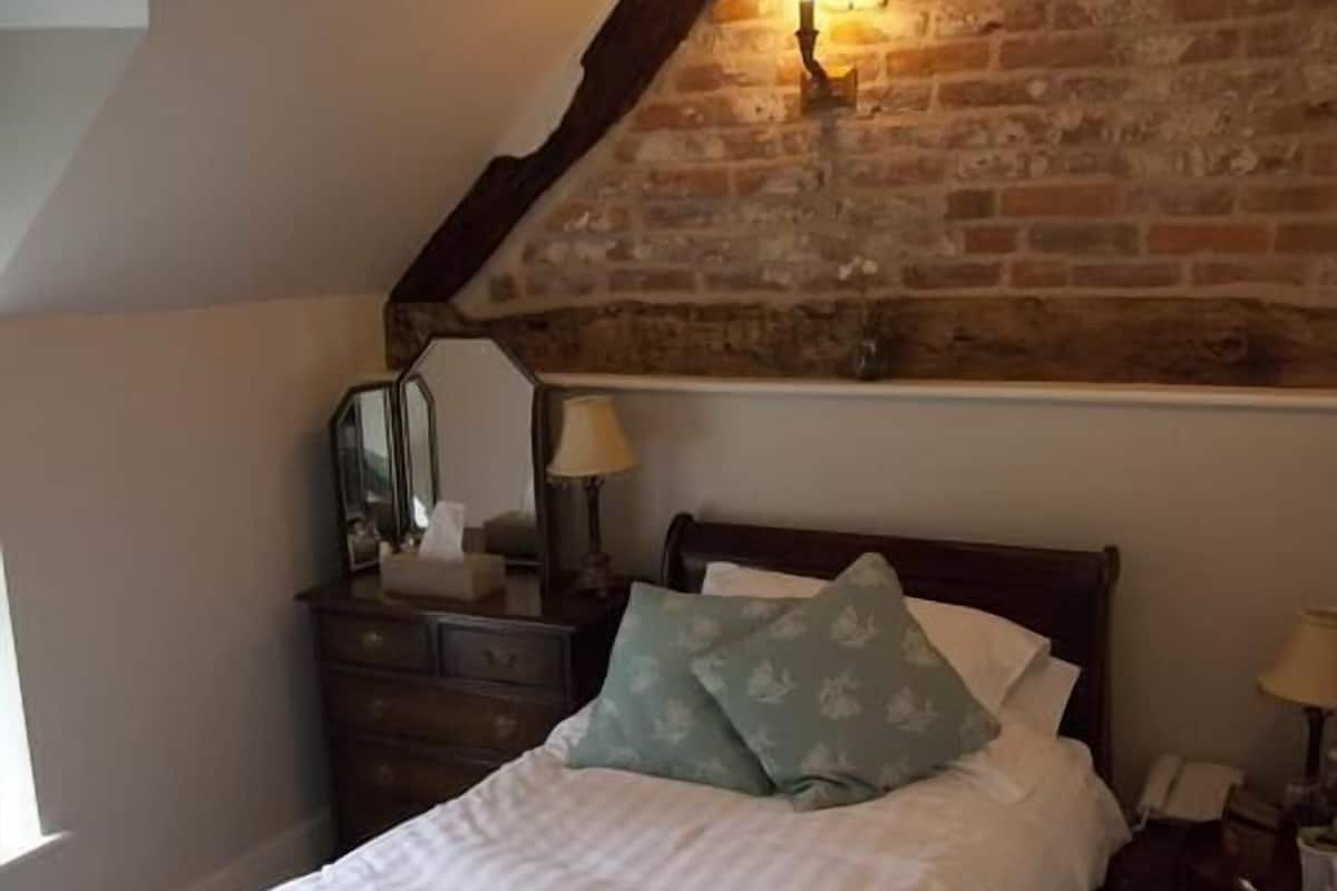 A bedroom with a sloped ceiling, a wooden headboard, a bed with pillows, a nightstand, a lamp, and a dresser with a mirror.