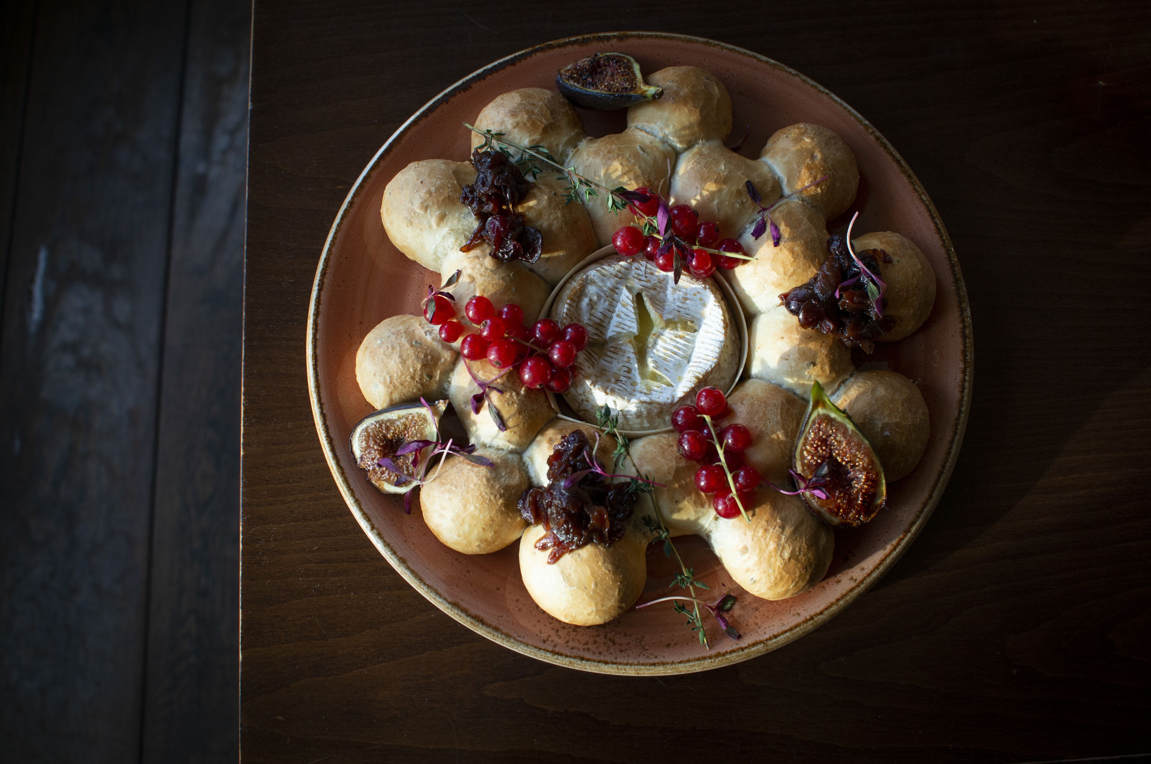 A round ceramic plate with small round pastries, some with dried fruits and herbs, and a small bowl of jam in the center.