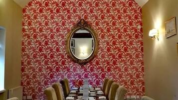 Comedor con mesa de madera preparada para seis comensales, papel tapiz estampado y un espejo sobre la mesa.
