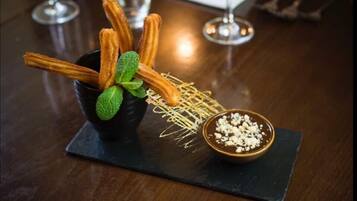 Un plat de postres amb xurros, una fulla de menta i un bol de salsa de xocolata sobre una placa de pedra.