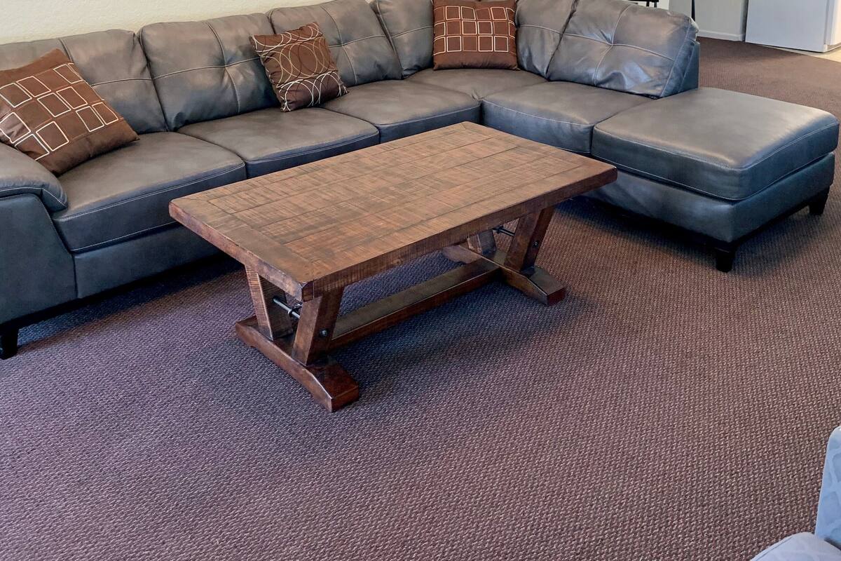 Un salon avec un canapé d’angle, une table basse en bois et des œuvres d’art abstraites accrochées au mur.