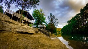 Un edificio a la orilla del río con un muro de contención de piedra, un espacio de estar al aire libre cubierto y vistas al río.