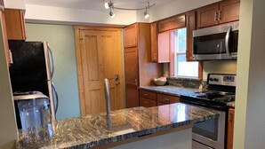 A kitchen with granite countertops, wooden cabinets, stainless steel appliances, and a black refrigerator. - Park Right by Your Door -1 BR, 1 Bath, Full Kitchen, 1st Floor Laundry. (Lansing)
