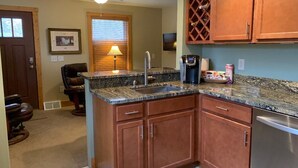 A kitchen with wooden cabinets, a granite countertop, a stainless steel dishwasher, and a ceiling fan. - Park Right by Your Door -1 BR, 1 Bath, Full Kitchen, 1st Floor Laundry. (Lansing)