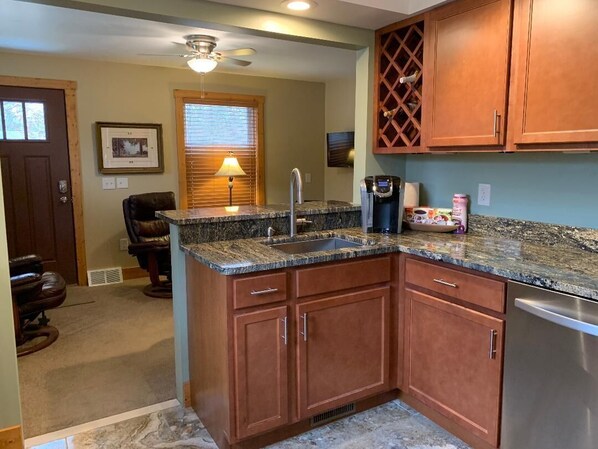 A kitchen with wooden cabinets, a granite countertop, a stainless steel dishwasher, and a ceiling fan. - Park Right by Your Door -1 BR, 1 Bath, Full Kitchen, 1st Floor Laundry. (Lansing)