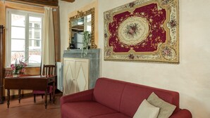 Ein Wohnzimmer mit einem roten Sofa, einem Holztisch mit Stühlen, einem Spiegel und einem großen Wandteppich mit Blumenmuster.
