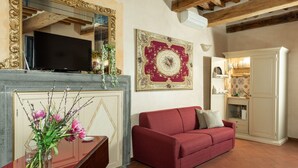Ein Wohnzimmer mit rotem Sofa, einem Fernseher auf einem Kaminbrett, einem dekorativen Spiegel und einem Wandbehang mit rotem und goldenem Muster.