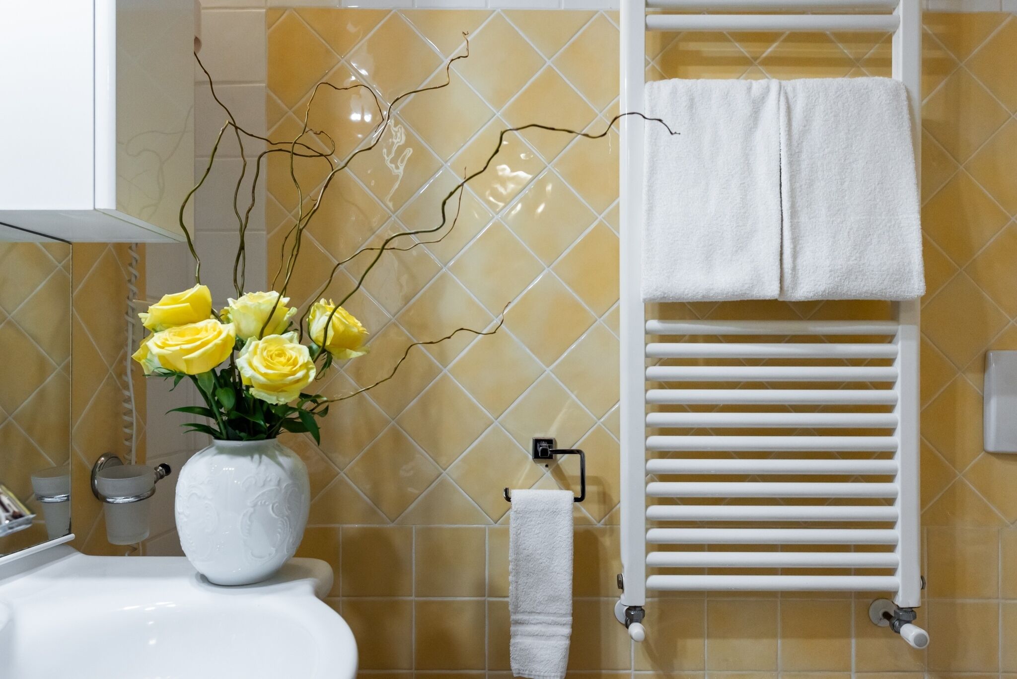 A bathroom with a white sink, a vase with yellow flowers, a white towel rack, and a white towel.