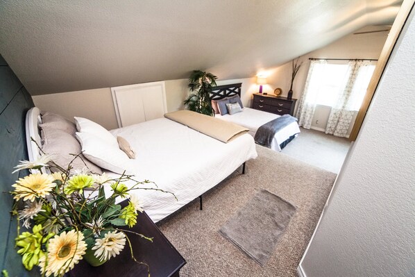 A bedroom with two beds, a bedside table with a lamp, a potted plant, and a window with curtains.