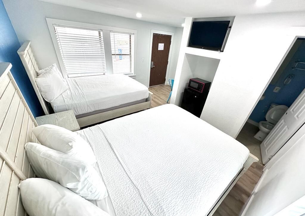 Quarto com uma cama grande, televisão na parede e uma pequena área de cozinha.