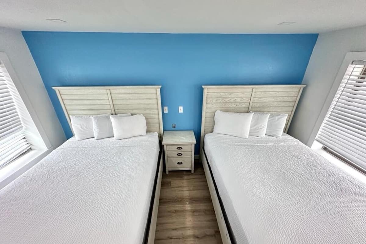 A room with two beds, a small bedside table, and a blue wall.