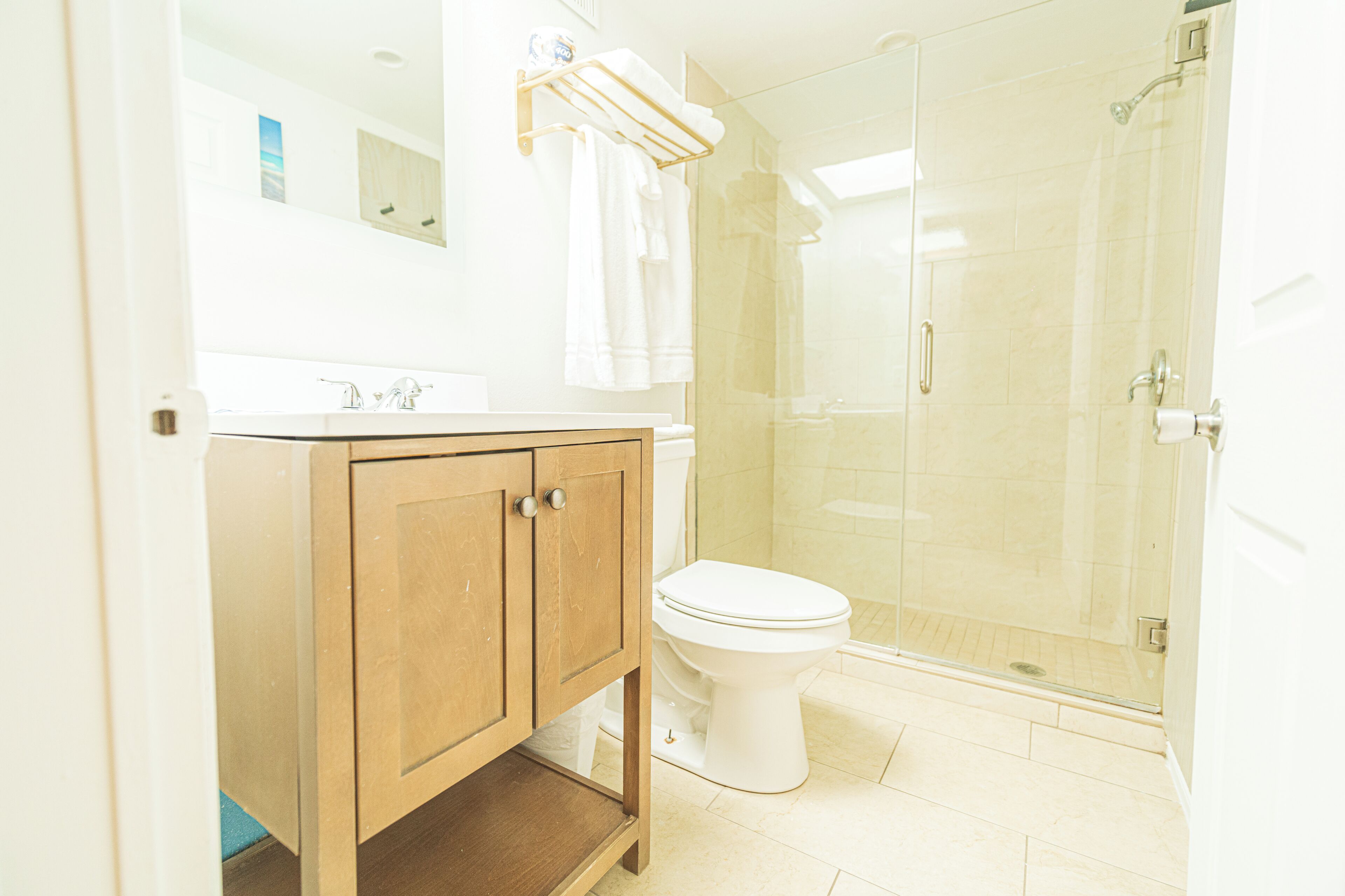 Un baño con tocador de madera, inodoro y zona de ducha con mampara de vidrio.