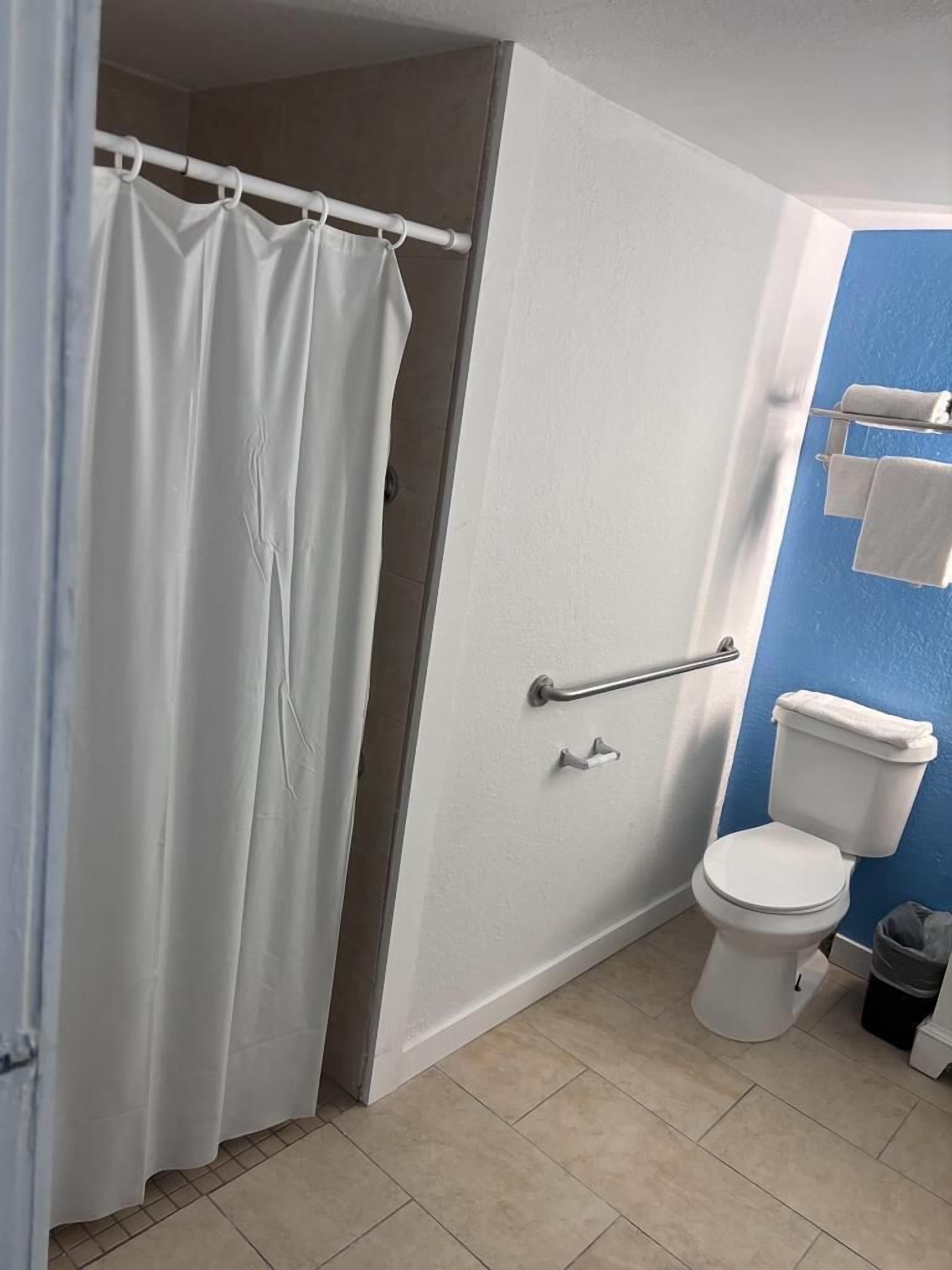 A bathroom with a white toilet, a shower curtain, a grab bar, and a towel rack.