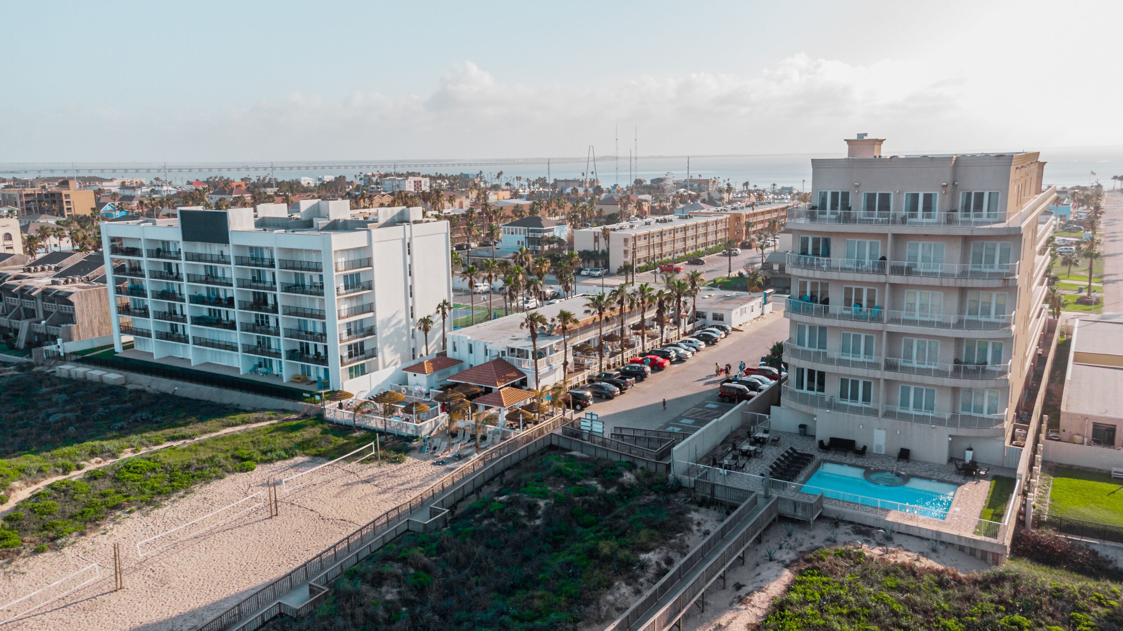 A coastal hotel with multiple floors, a swimming pool, and a beach area.