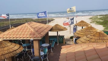 Een restaurant aan het strand met rieten parasols en terras.