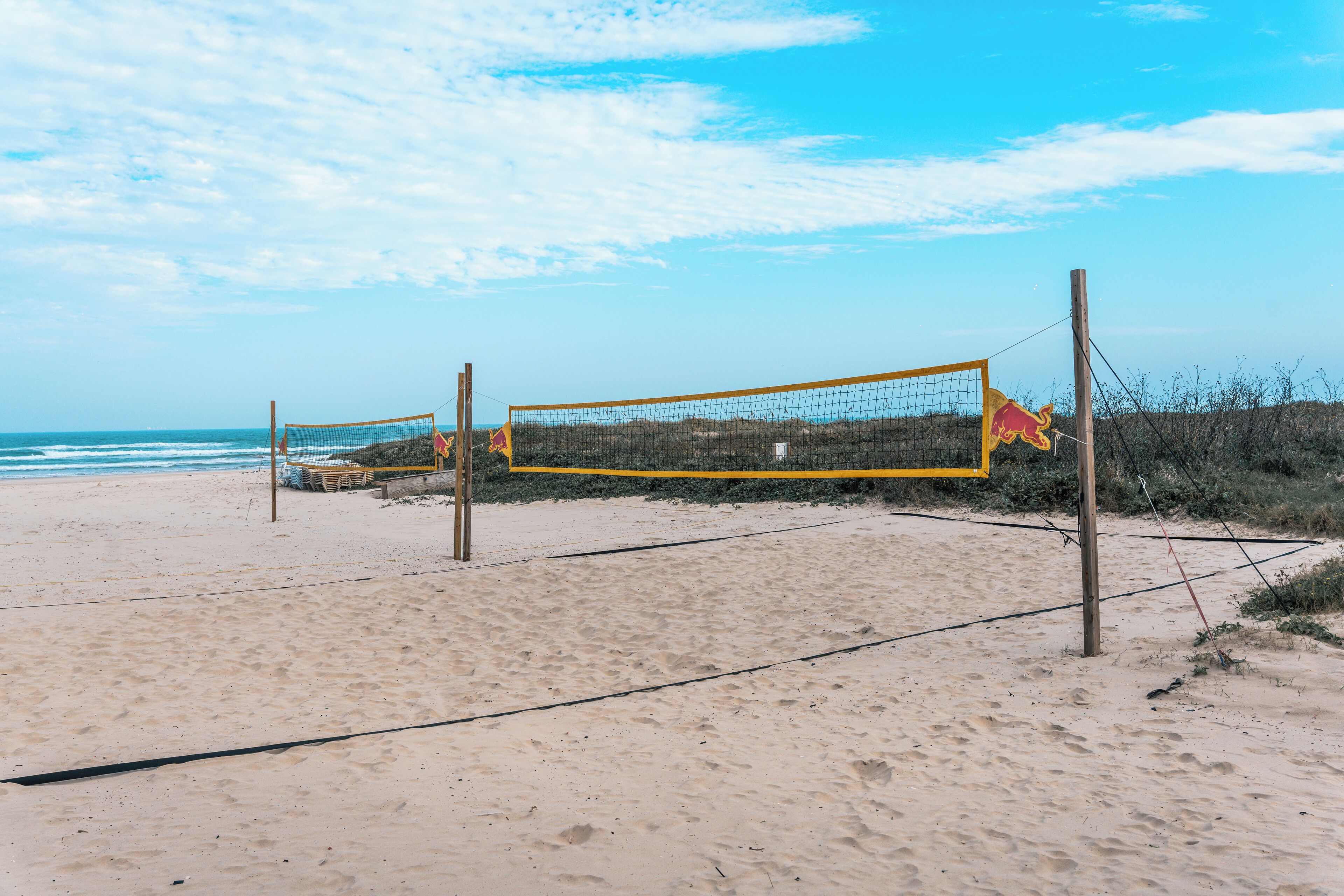 Ein Beachvolleyballnetz an einem Sandstrand, im Hintergrund das Meer.