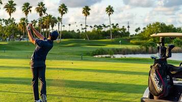 A golf course with a player in mid-swing, palm trees, and a golf cart in the background.