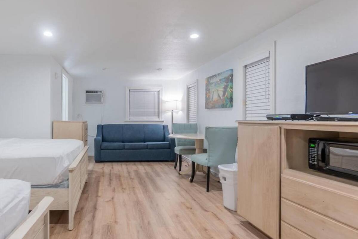 A hotel room with two beds, a sofa, a small table, a TV, and a microwave.