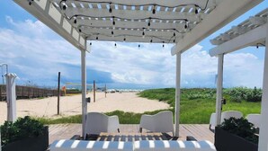 A covered outdoor seating area with a view of a beach and dunes. - Coco Beach Hotel on South Padre Island (South Padre Island)