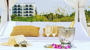 A beachside bed with a canopy, a bottle of champagne, and two glasses on a tray. - Coco Beach Hotel on South Padre Island (South Padre Island)