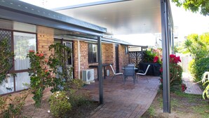 A covered patio area with brick walls, a table, chairs, and a small garden with flowering plants. - Wellington Parade 15a, Shelly Beach, Caloundra (SHELLY BEACH)