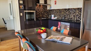Een moderne keuken met donkere kastjes, een betegelde spatwand, roestvrijstalen apparatuur en een eetgedeelte met een tafel, stoelen en een fruitschaal.