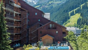 Ein mehrstöckiges Hotel mit Balkonen, einem Pool und einer Bergkulisse.