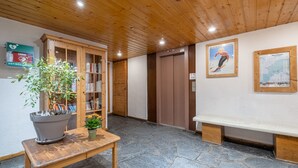 A reception area with a wooden bench, a potted plant, a bookshelf, and an elevator. -  Résidence Pierre & Vacances Résidence Le Peillon (Les Allues)