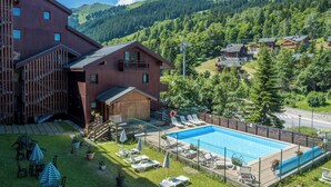 A wooden building with a pool, surrounded by a fenced area with lounge chairs and umbrellas. -  Résidence Pierre & Vacances Résidence Le Peillon (Les Allues)
