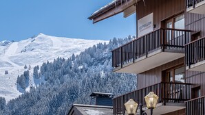 A hotel with a balcony, a sign reading "Le Peillon," and a snowy mountain backdrop. -  Résidence Pierre & Vacances Résidence Le Peillon (Les Allues)