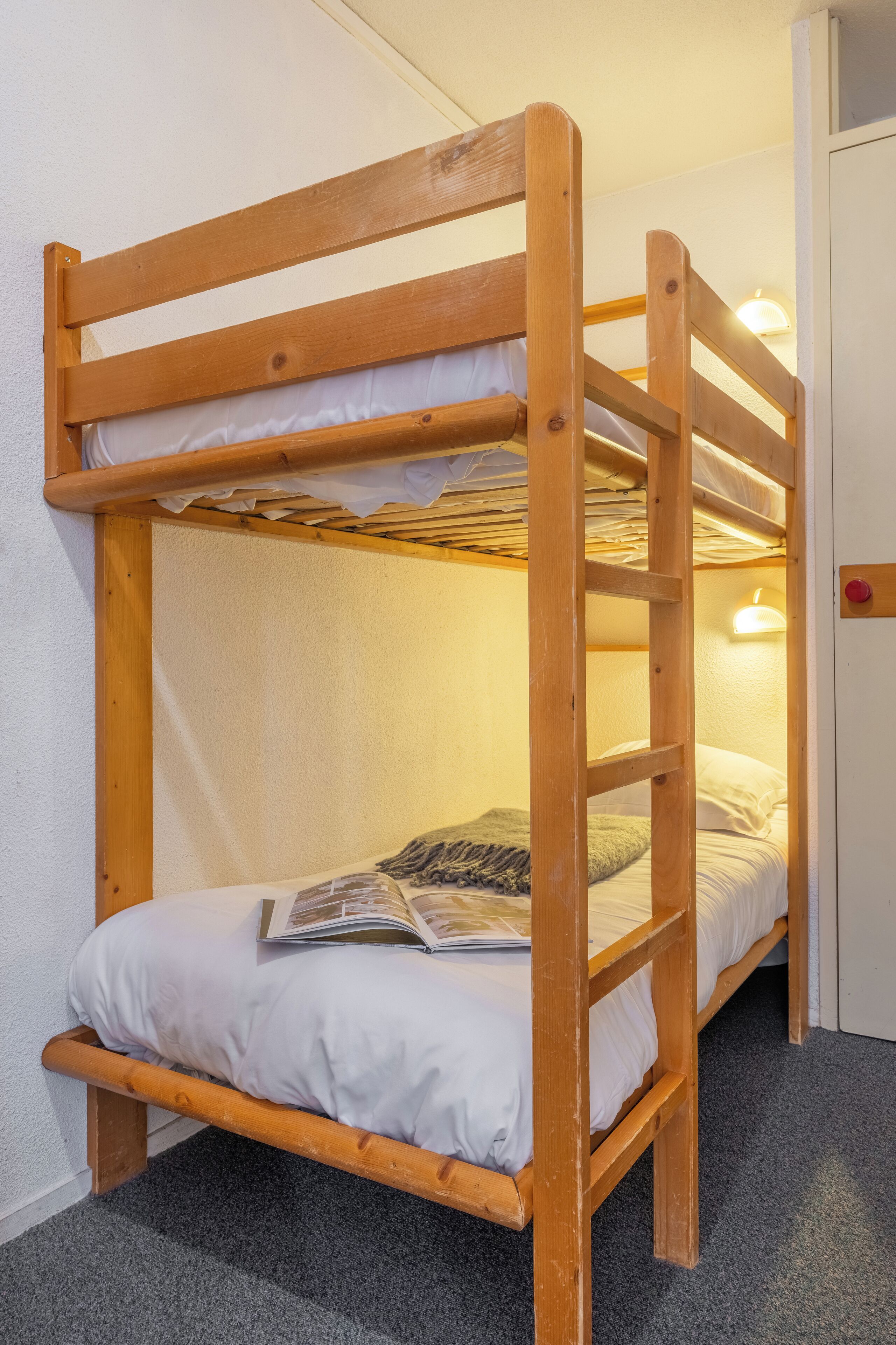 Un lit superposé avec une échelle, une porte avec une poignée rouge et un luminaire fixé au mur.