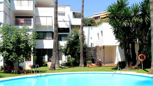 A swimming pool surrounded by a white building with balconies, palm trees, and a lifebuoy. - Marbella apartment with swimming pool (Marbella)