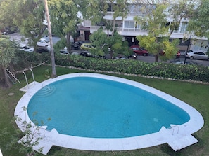 A residential swimming pool with a curved edge, surrounded by a grassy lawn and a hedge. - Marbella apartment with swimming pool (Marbella)