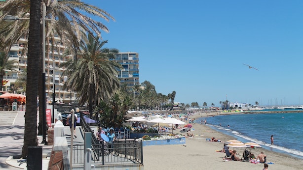 A beach with palm trees, umbrellas, and people. - Marbella apartment with swimming pool (Marbella)