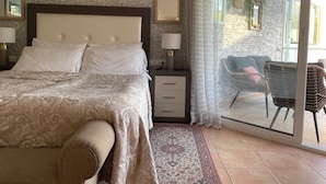 A bedroom with a bed, bedside tables, a nightstand, a patterned rug, and a view of an outdoor area with a chair and a table. - Marbella apartment with swimming pool (Marbella)