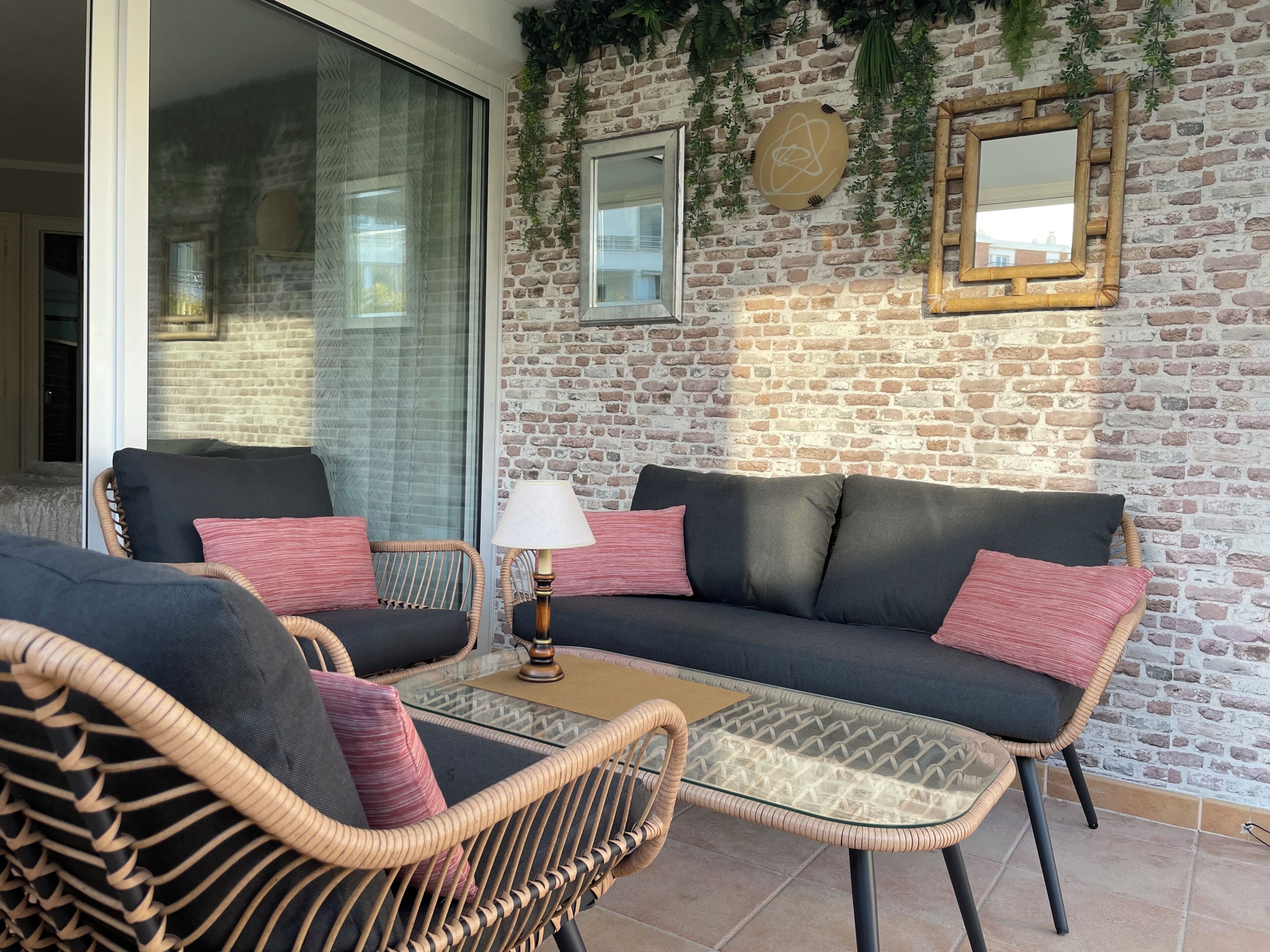 A cozy outdoor seating area with wicker furniture, a glass-top table, and a brick wall backdrop.