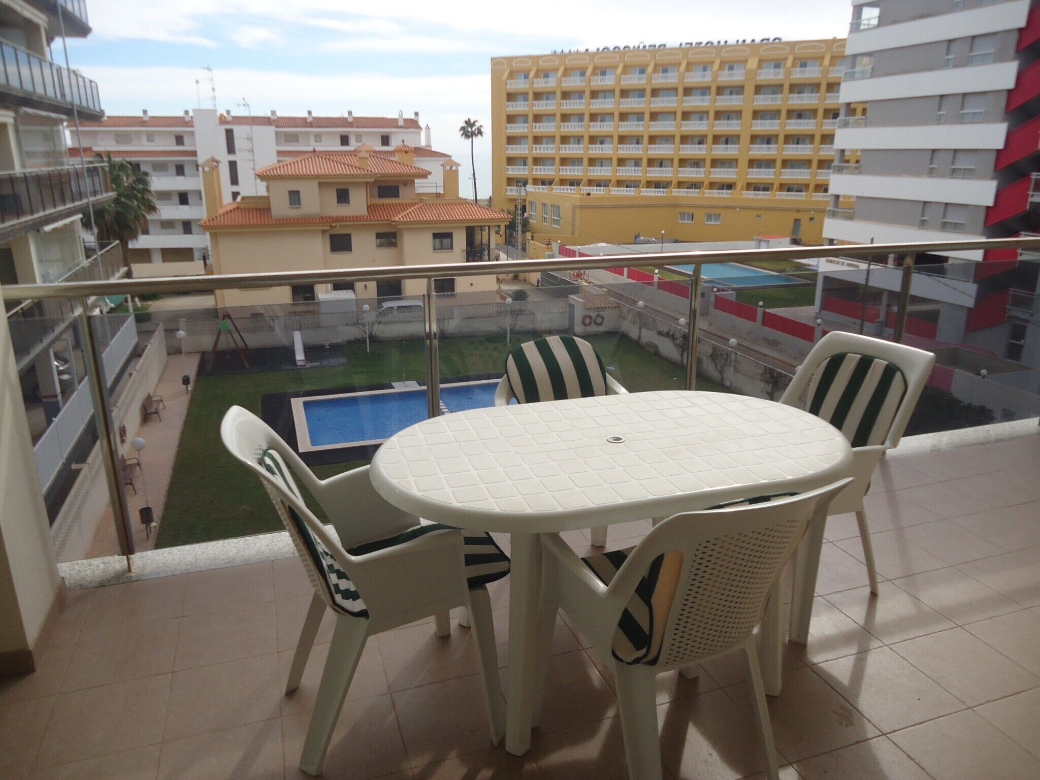Un balcon doté d’une table ronde et de quatre chaises, offrant une vue sur une piscine et les bâtiments avoisinants.